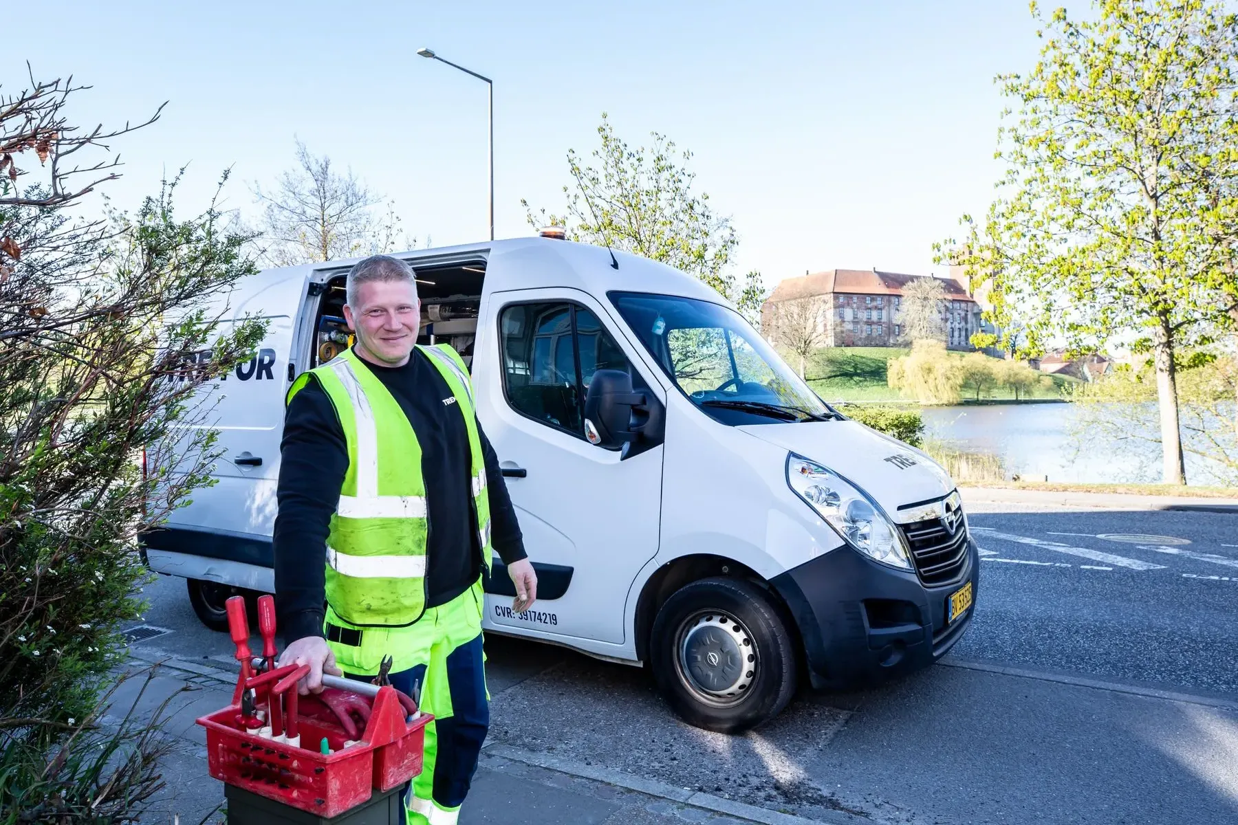 Servicetechniker in Warnweste trägt einen Werkzeugkasten vor seinem Transporter